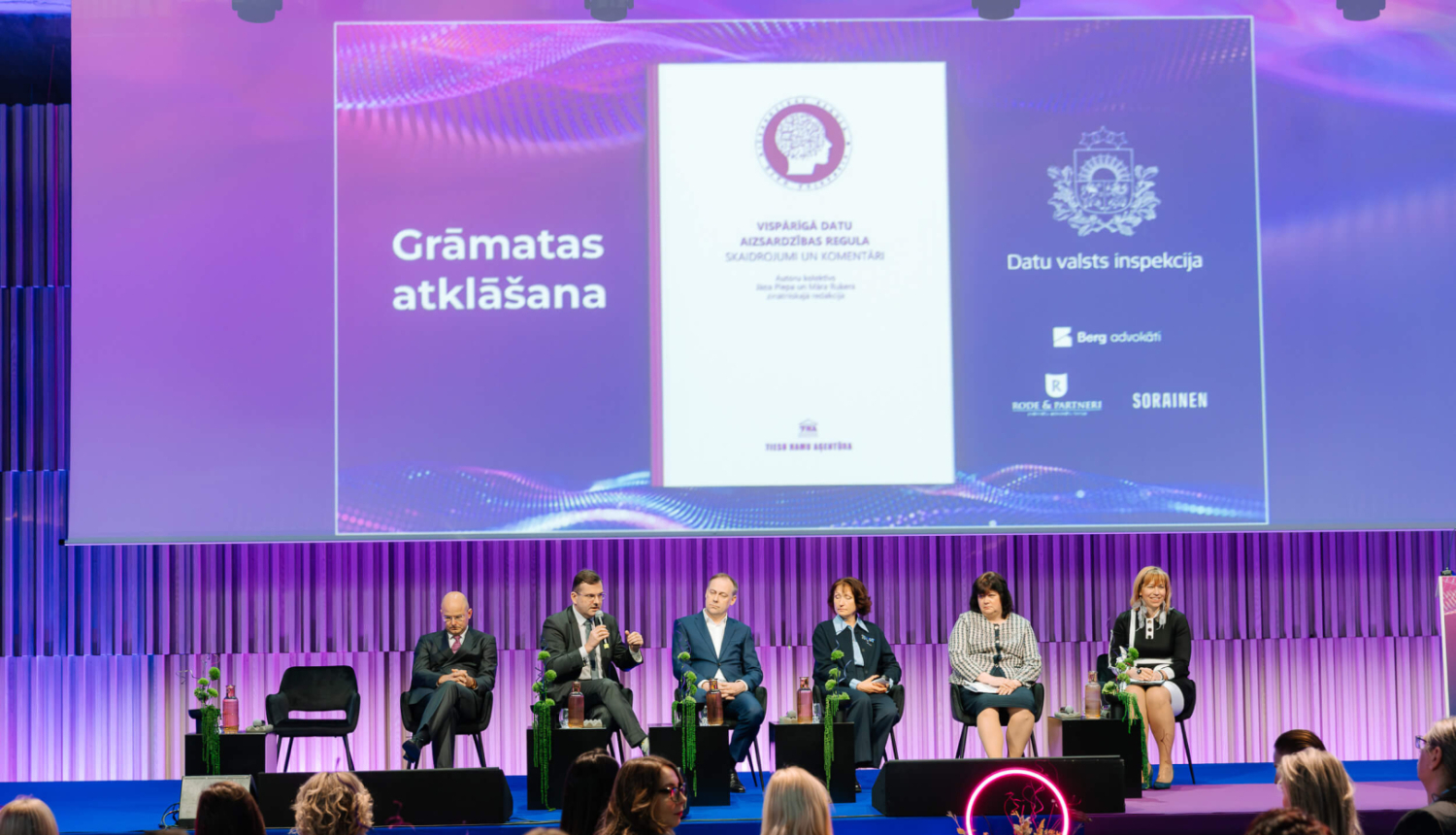 Grāmatas atklāšanas pasākums. Fonā redzams prezentācijas ekrāns ar grāmatas vāku un Datu valsts inspekcijas logo, priekšplānā - auditorija.