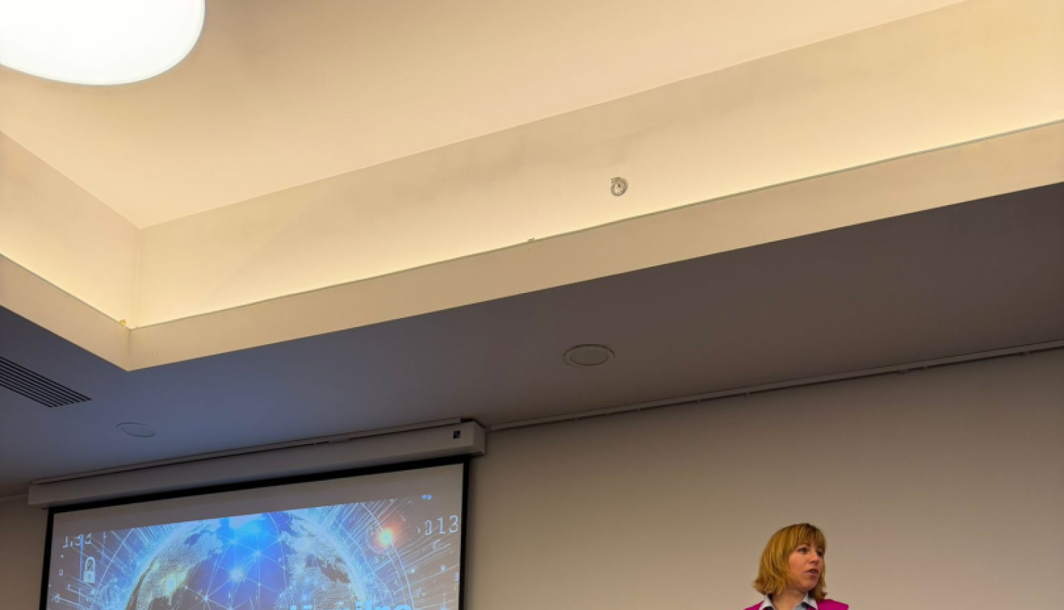 Datu valsts inspekcijas direktore uzstājas Latvijas Iekšējo auditoru institūta konferencē ar prezentāciju “Ilgtspējīga un jēgpilna personas datu aizsardzības sistēma”. Fonā redzams prezentācijas slaids ar globusa un datu tīkla vizualizāciju.