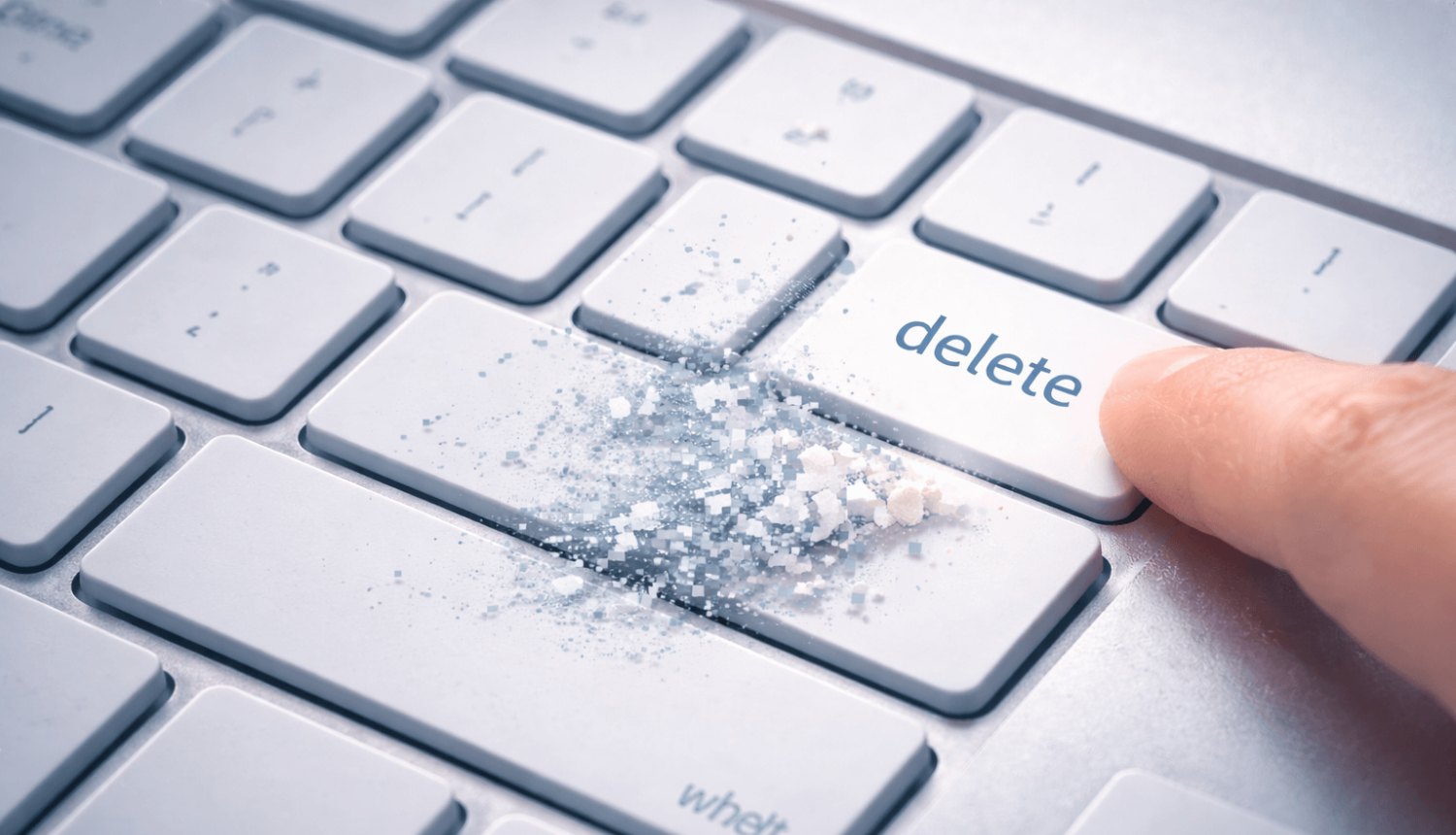 Tuvplānā redzama sudrabotas krāsas datora tastatūra, kur pirksts nospiež taustiņu ar uzrakstu “delete”.